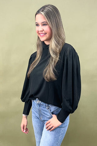 Woman wearing a black top and blue jeans against a green background