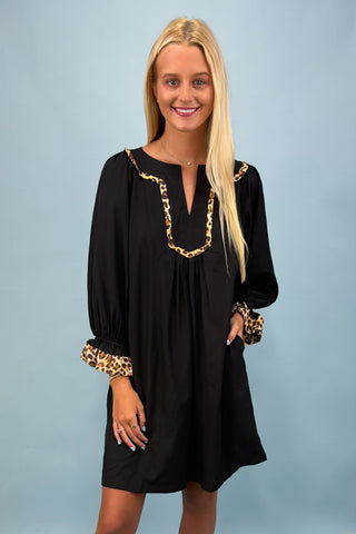 Woman wearing a black dress with gold accents against a light blue background