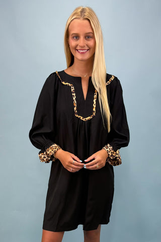 Woman wearing a black dress with gold chain details and leopard print cuffs against a light blue background