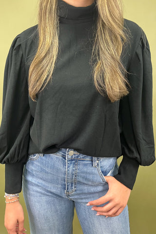 Woman wearing a black top and blue jeans against a green background