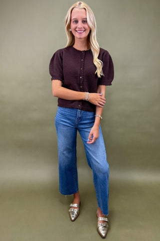 Woman wearing a dark brown blouse and blue jeans against a green background