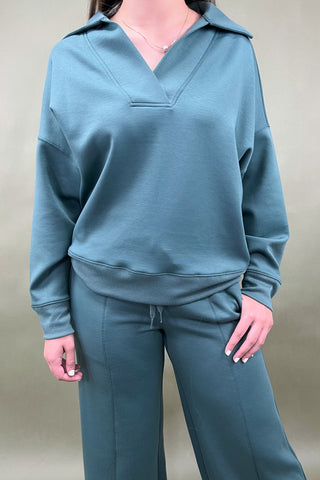 Person wearing a teal sweatshirt and pants against a plain background