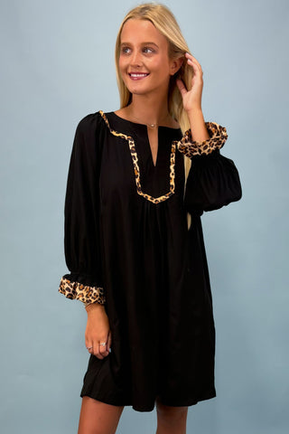 Woman wearing a black dress with leopard print cuffs against a gray background