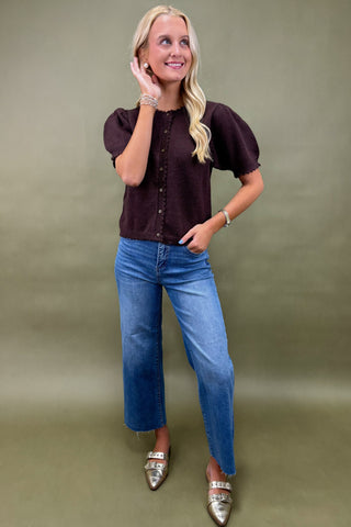 Woman wearing a brown blouse and blue jeans against a green background