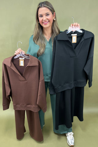Woman holding two sweatshirts, one brown and one black, on hangers against a green background.