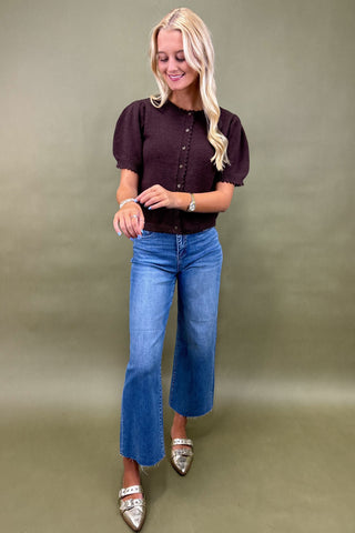 Woman wearing a dark blouse and blue jeans against a plain background