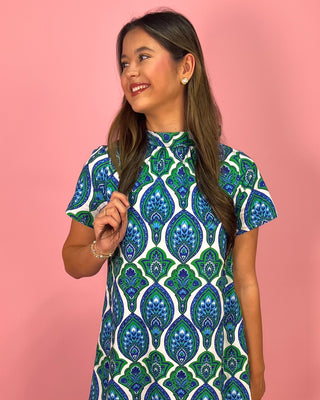 Girl wearing a blue and green patterned dress against a pink background