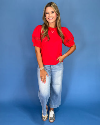 Woman wearing a red top and blue jeans against a blue background