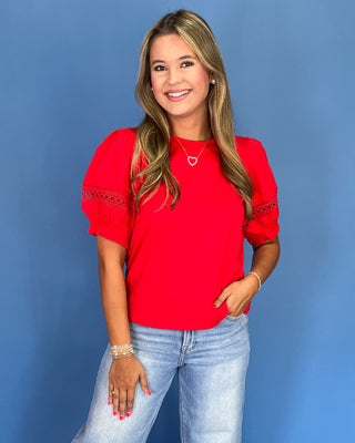 Woman wearing a red blouse with lace details and light blue jeans against a blue background