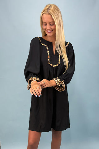 Woman wearing a black dress with gold accents against a light blue background