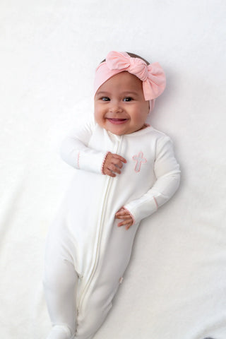 Baby in a white onesie with a pink bow headband on a white background