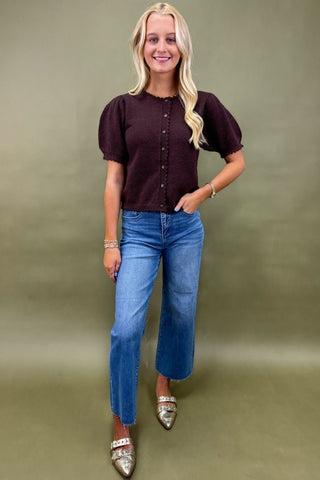 Woman wearing a brown top and blue jeans against a green background