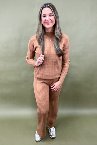 Woman wearing a brown ribbed sweater and pants set against a green background