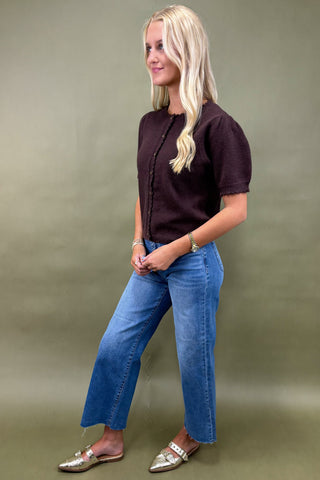 Woman wearing a dark brown top and blue jeans against a green background