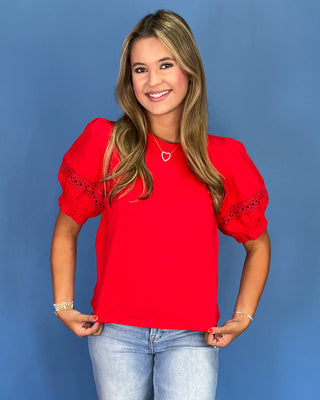 Woman wearing a red blouse with lace details on a blue background