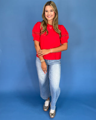 Woman wearing a red top and light blue jeans against a blue background