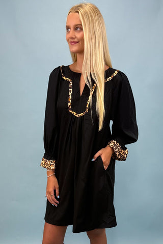 Woman wearing a black dress with leopard print accents on a light blue background