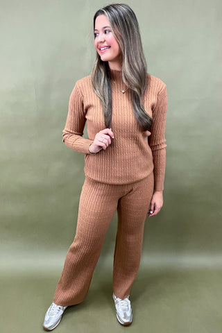 Woman wearing a brown ribbed sweater and pants set against a green background