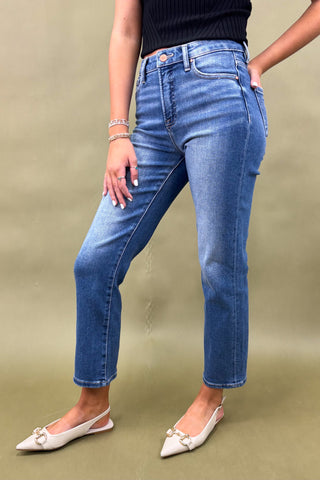 Person wearing blue jeans and white shoes on a beige background