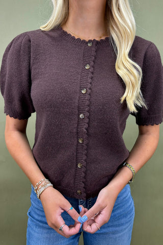 Person wearing a brown knitted cardigan with short sleeves against a green background