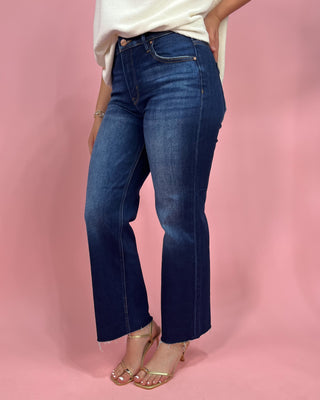 Person wearing blue jeans and a white top on a pink background