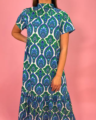 Person wearing a blue and green patterned dress against a pink background