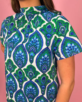 Person wearing a shirt with a blue and green pattern on a pink background