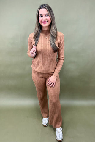 Woman wearing a brown ribbed sweater and pants set against a green background