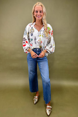 Woman wearing a colorful blouse, blue jeans, and silver shoes against a green background