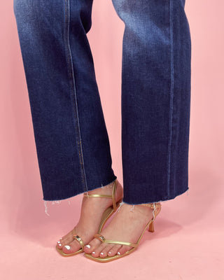 Close-up of blue jeans and gold sandals on a pink background