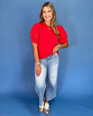 Woman wearing a red top and blue jeans against a blue background