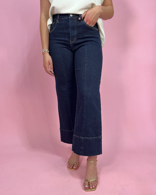 Person wearing dark blue jeans on a pink background