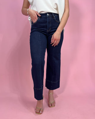 Person wearing dark blue jeans and a white top on a pink background
