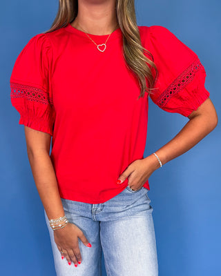 Person wearing a red blouse with lace sleeves against a blue background