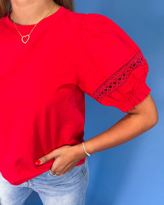 Red blouse with lace details on sleeves against a blue background