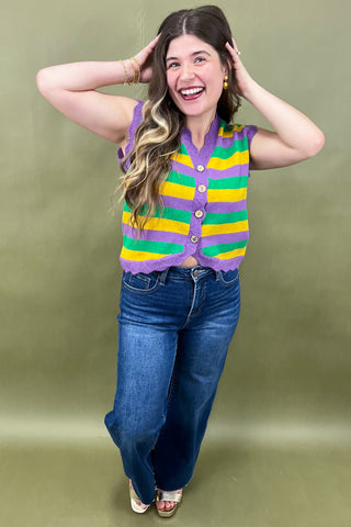 Woman wearing a colorful striped sweater vest and blue jeans against a green background