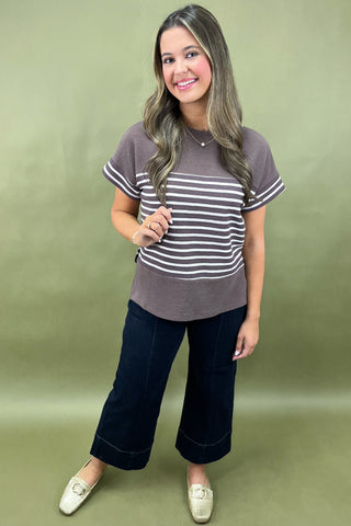 Woman wearing a striped shirt and dark pants against a green background