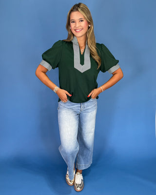 Woman wearing a green blouse with gray accents and blue jeans on a blue background