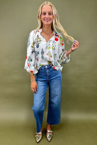 Woman wearing a colorful blouse and blue jeans against a green background