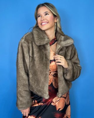 Taupe faux fur cropped jacket with plush texture, oversized collar, long sleeves, and front zipper closure.