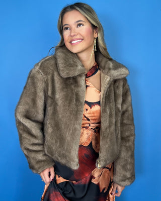 Taupe faux fur cropped jacket with plush texture, oversized collar, long sleeves, and front zipper closure.