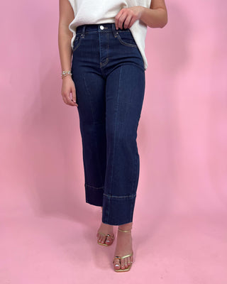 Person wearing dark blue jeans and a white top on a pink background