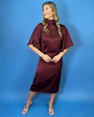Burgundy satin midi dress with a turtleneck, flutter sleeves, relaxed silhouette, and side slit detail.