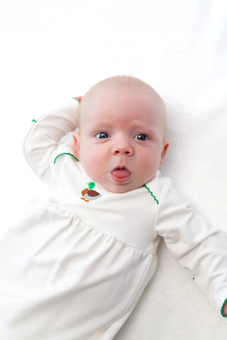 Baby in a white onesie with green accents lying on a white surface