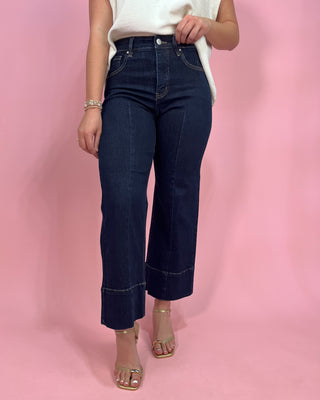 Person wearing dark blue jeans on a pink background