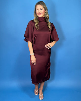 Burgundy satin midi dress with a turtleneck, flutter sleeves, relaxed silhouette, and side slit detail.
