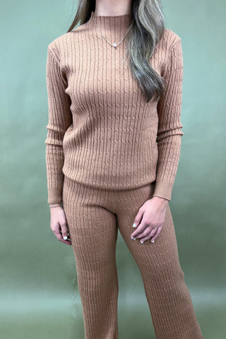 Person wearing a beige ribbed sweater and pants set against a light green background