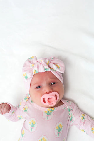 Newborn baby wearing a pink floral headband and matching outfit on a white background