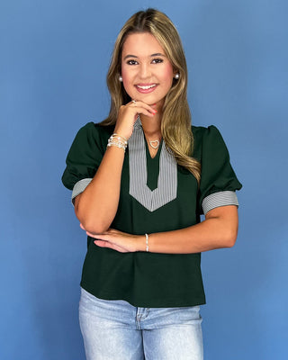 Woman wearing a green blouse with a striped collar against a blue background