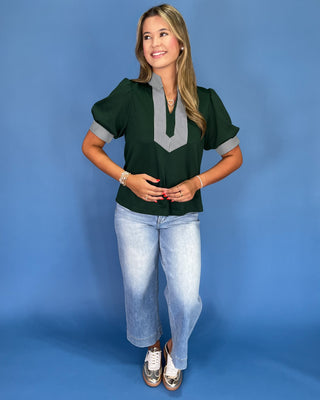 Woman wearing a green blouse with gray accents and light blue jeans on a blue background
